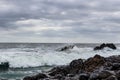 Surf on a rocky coast in front of the horizon under a cloudy sky. Tropical stormy ocean with waves crashing on the rocks. Royalty Free Stock Photo