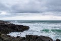 Surf on a rocky coast in front of the horizon under a cloudy sky. Tropical stormy ocean with waves crashing on the rocks. Royalty Free Stock Photo