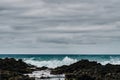 Surf on a rocky coast in front of the horizon under a cloudy sky. Tropical stormy ocean with waves crashing on the rocks. Royalty Free Stock Photo