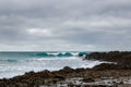 Surf on a rocky coast in front of the horizon under a cloudy sky. Tropical stormy ocean with waves crashing on the rocks. Royalty Free Stock Photo