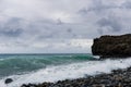 Surf on a rocky coast in front of the horizon under a cloudy sky. Tropical stormy ocean with waves crashing on the rocks. Royalty Free Stock Photo