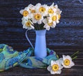 Bouquet of daffodils flowers in blue vase, colorful shawl on dark wooden background. Generated image