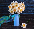 Bouquet of daffodils flowers in blue vase, colorful shawl on dark wooden background. Generated image