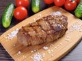 A freshly cooked juicy steak lies on a bamboo cutting board, coarse salt is scattered nearby