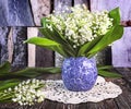 A bouquet of fresh lily of the valley flowers in a blue vase on a dark wooden background Royalty Free Stock Photo