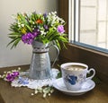 A bright bouquet of spring wildflowers with lilies of the valley in a vintage jug and a cup of coffee on the window Royalty Free Stock Photo