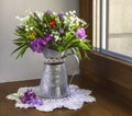 A bright bouquet of spring wildflowers with lilies of the valley in a vintage jug on a window in sunlight. Royalty Free Stock Photo