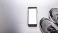 A smartphone with white screen and sneekers on metal background Royalty Free Stock Photo