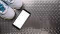 A smartphone with white screen and sneekers on metal background Royalty Free Stock Photo