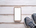 A smartphone with white screen and sneekers on wooden background Royalty Free Stock Photo