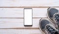 A smartphone with white screen and sneekers on wooden background Royalty Free Stock Photo