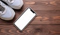 A smartphone with white screen and sneekers on wooden background Royalty Free Stock Photo