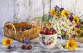 Summer still life with a basket of cherries, a cup with cherries and a bouquet of summer wildflowers Royalty Free Stock Photo