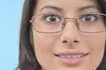 Extreme close-up of woman with glasses smiling slightly and looking directly at camera against soft blue background Royalty Free Stock Photo