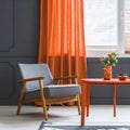 Grey armchair at orange table in dark retro living room interior with drapes Royalty Free Stock Photo