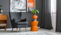 Grey armchair at orange table in dark retro living room interior with drapes Royalty Free Stock Photo