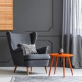 Grey armchair at orange table in dark retro living room interior with drapes Royalty Free Stock Photo
