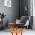 Grey armchair at orange table in dark retro living room interior with drapes Royalty Free Stock Photo