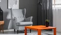 Grey armchair at orange table in dark retro living room interior with drapes Royalty Free Stock Photo