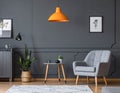 Orange lamp above table and grey armchair in dark vintage living room interior Royalty Free Stock Photo