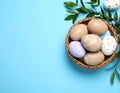 Beautiful decorated Easter eggs and wicker bowl on light blue background, flat lay Royalty Free Stock Photo