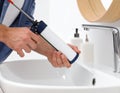 Man with caulking gun sealing washbasin in bathroom, closeup. Royalty Free Stock Photo