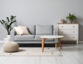 Soft sofa, coffee table, pouf, houseplants and chest of drawers near grey wall in live room Royalty Free Stock Photo