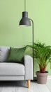 Stylish sofa with pillow, houseplant and lamp near green wall indoors Royalty Free Stock Photo