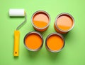 Cans of orange paint and roller brush on green background, flat lay. Royalty Free Stock Photo