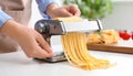 Woman preparing noodles with pasta maker machine at table indoors, closeup Royalty Free Stock Photo
