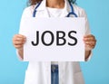 Woman holding sheet of paper with word JOBS on blue background, closeup. Career Royalty Free Stock Photo