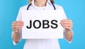 Woman holding sheet of paper with word JOBS on blue background, closeup. Career Royalty Free Stock Photo