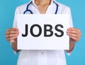 Woman holding sheet of paper with word JOBS on blue background, closeup. Career Royalty Free Stock Photo
