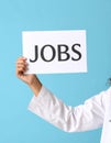 Woman holding sheet of paper with word JOBS on blue background, closeup. Career Royalty Free Stock Photo