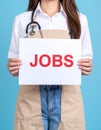 Woman holding sheet of paper with word JOBS on blue background, closeup. Career Royalty Free Stock Photo
