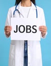 Woman holding sheet of paper with word JOBS on blue background, closeup. Career Royalty Free Stock Photo