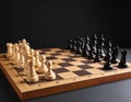 Many chess pieces on wooden checkerboard against black background, selective focus Royalty Free Stock Photo