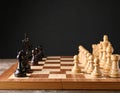 Many chess pieces on wooden checkerboard against black background, selective focus Royalty Free Stock Photo