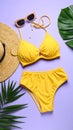 Flat lay composition with yellow swimsuit, hat and sunglasses on purple background Royalty Free Stock Photo