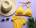 Flat lay composition with yellow swimsuit, hat and sunglasses on purple background Royalty Free Stock Photo