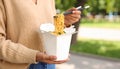 Woman eating takeaway noodles from paper box with fork outdoors, closeup. Street food Royalty Free Stock Photo