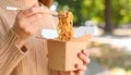 Woman eating takeaway noodles from paper box with fork outdoors, closeup. Street food Royalty Free Stock Photo