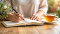 Hands journaling in open notebook with herbal tea, warm neutral tones Royalty Free Stock Photo