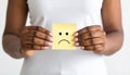 Woman holding sticky note with drawn sad face and suffering from cystitis on white Royalty Free Stock Photo