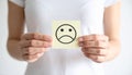 Woman holding sticky note with drawn sad face and suffering from cystitis on white Royalty Free Stock Photo