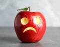 Apple with crying face on grey table, closeup. Concept of jealousy Royalty Free Stock Photo