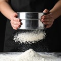 Woman sifting wheat flour at table against black background, closeup Royalty Free Stock Photo