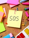 Note with word SOS and stationery on cork board, closeup Royalty Free Stock Photo