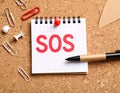 Note with word SOS and stationery on cork board, closeup Royalty Free Stock Photo