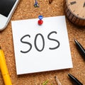 Note with word SOS and stationery on cork board, closeup Royalty Free Stock Photo